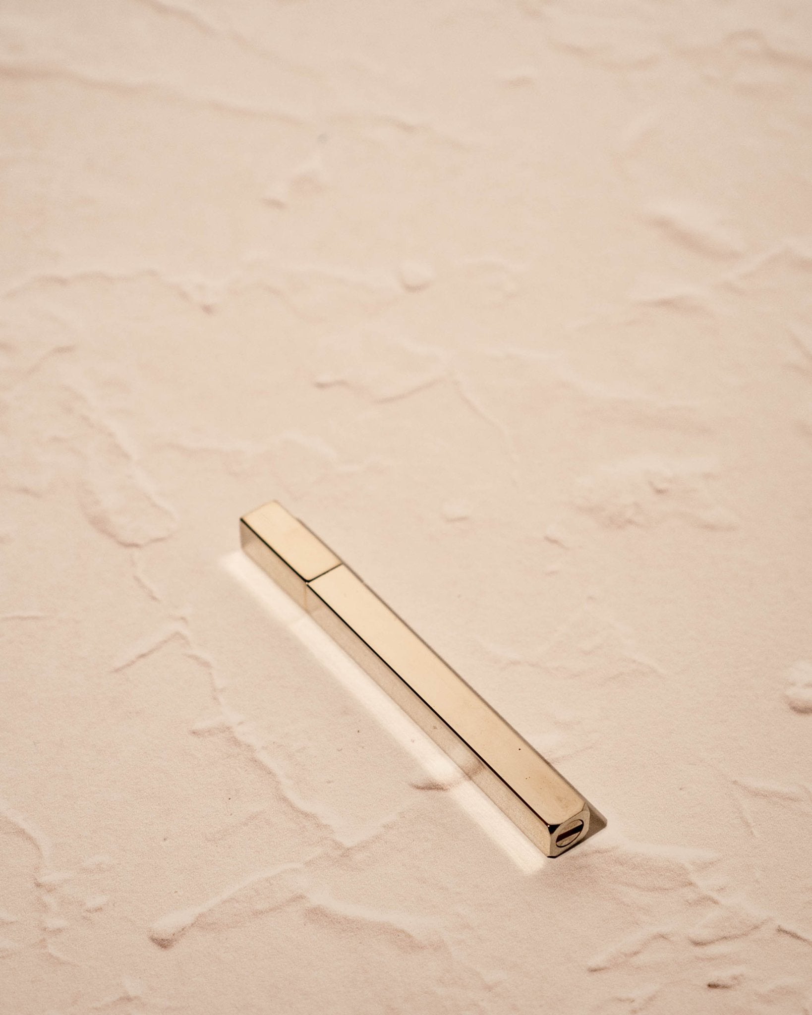 silver toned Queue Lighter by Tsubota Pearl in gold finish on textured beige surface