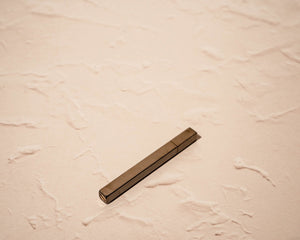 Gunmetal stick lighter by Tsubota Pearl with slim rectangular profile, resting on side.

